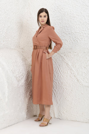 Woman wearing a midi linen dress against a textured white wall.