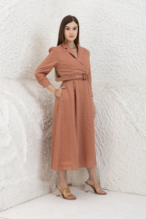 Woman wearing a midi linen dress against a textured white wall.