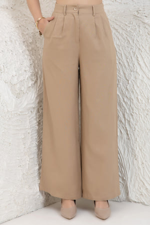Beige wide-leg pants worn by a women against a textured white wall.