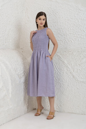 Woman wearing a light purple dress against a textured white wall.