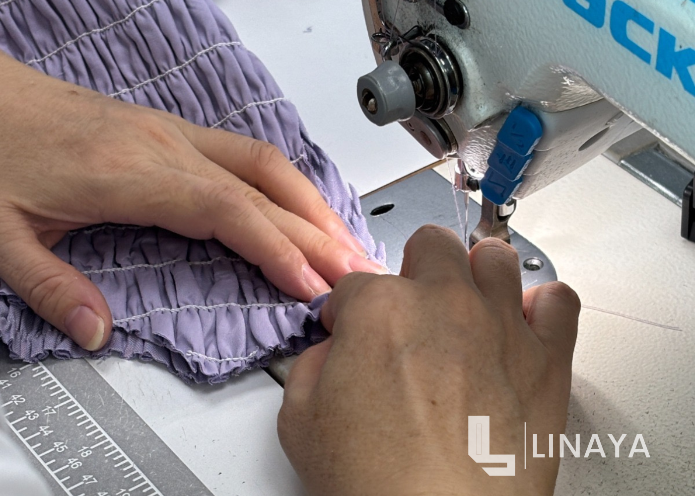 Person using a sewing machine on purple fabric with LINAYA branding.