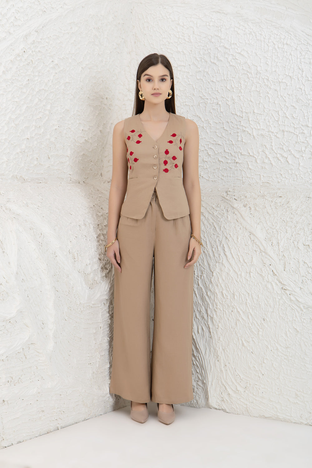 Woman wearing a beige sleeveless top with red heart patterns and matching pants against a textured white wall.