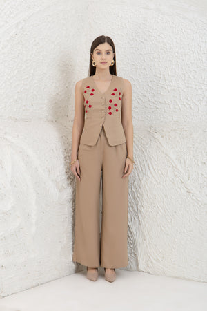 Woman wearing a beige linen vest with red heart patterns against a textured white wall.