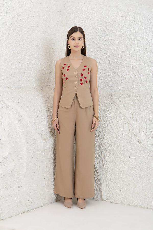 Woman wearing a beige linen vest with red heart patterns against a textured white wall.