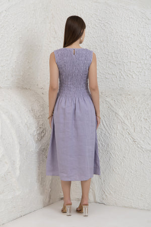 Woman wearing a light purple dress against a textured white wall.