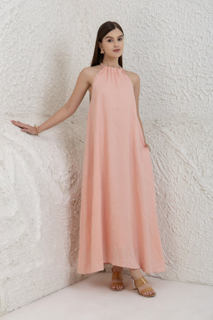 Woman wearing a long pink dress against a textured white wall.