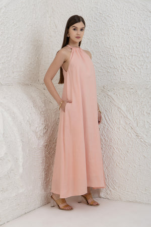 Woman wearing a pink halter neck dress against a textured white wall.