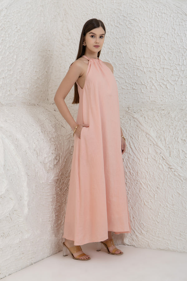 Woman wearing a pink halter neck dress against a textured white wall.