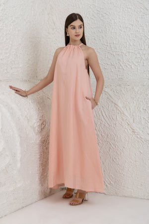 Woman wearing a pink halter neck dress against a textured white wall.