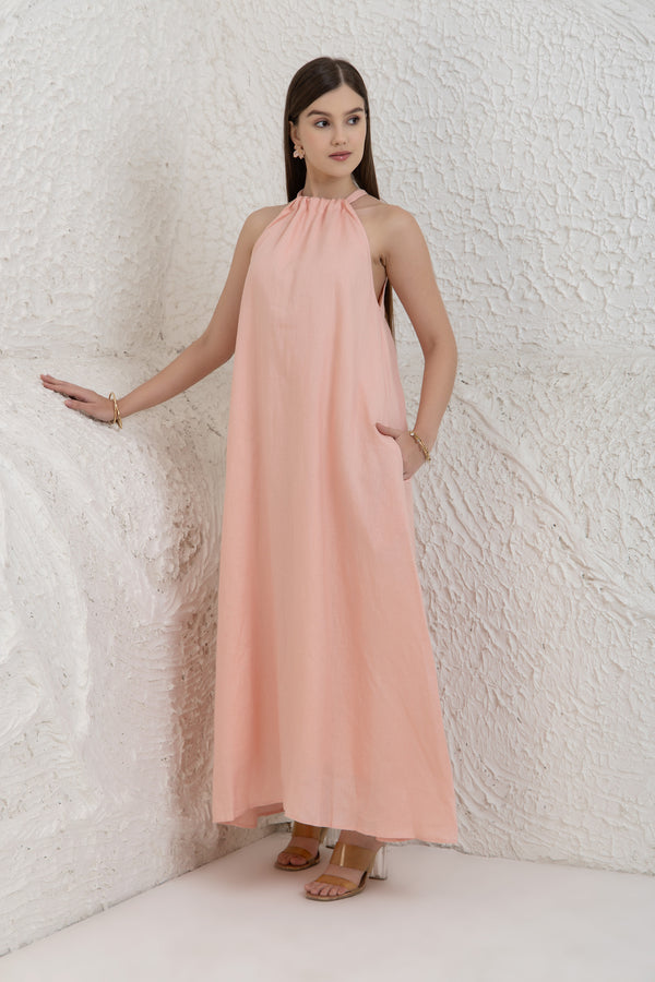 Woman wearing a pink halter neck dress against a textured white wall.