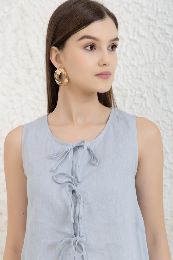 Woman wearing a terracotta midi linen wrap dresses sleeveless top with a textured white background