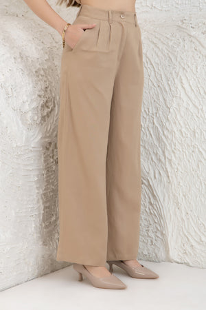 Person wearing beige wide-leg pants against a textured white wall.